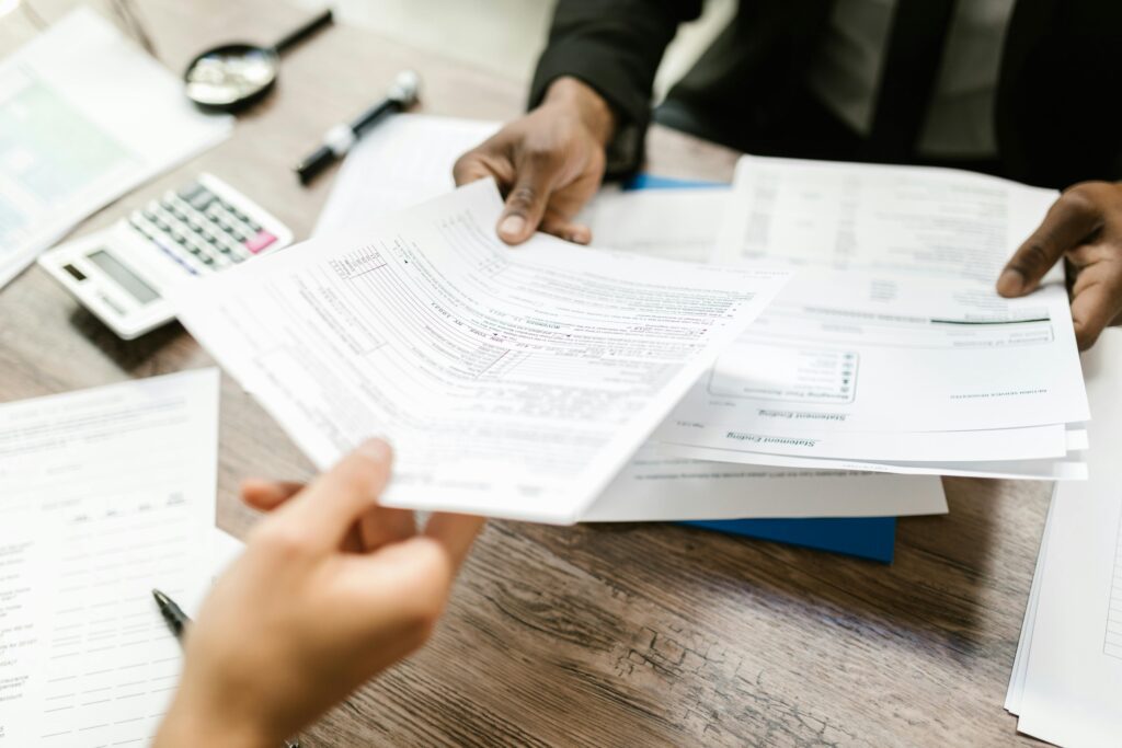 Main tendant un document fiscal à une autre personne, sur une table avec calculatrice et stylo